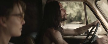 Movie still from “Hesher” (2010), directed by Spencer Susser – A man with long black hair smoking a cigarette while looking out a window; Close Up shot, Low angle