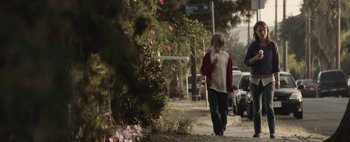 Movie still from “Hesher” (2010), directed by Spencer Susser – A young boy walking down a sidewalk next to flowers; Wide shot, Over the shoulder angle