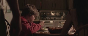 Movie still from “Hesher” (2010), directed by Spencer Susser – A young boy sitting at a table eating food; Medium shot, Over the shoulder angle