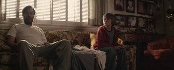 Movie still from “Hesher” (2010), directed by Spencer Susser – A boy sitting on a couch in a living room; Medium shot, Over the shoulder angle
