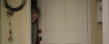 Movie still from “Hesher” (2010), directed by Spencer Susser – A young boy standing in front of a white door; Medium shot, Over the shoulder angle