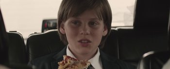 Movie still from “Hesher” (2010), directed by Spencer Susser – A boy in a suit and tie eating a piece of pizza; Close Up shot, Over the shoulder angle