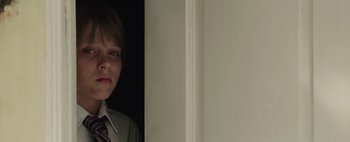 Movie still from “Hesher” (2010), directed by Spencer Susser – A young boy in a tie standing in front of a door; Close Up shot, Over the shoulder angle