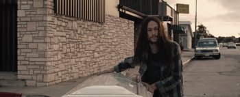 Movie still from “Hesher” (2010), directed by Spencer Susser – A man with long hair leaning on the hood of a car; Medium shot, High angle