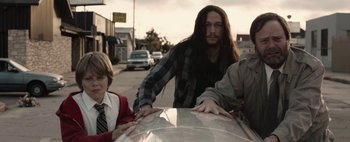 Movie still from “Hesher” (2010), directed by Spencer Susser – A man with long hair leaning on the hood of a car; Medium shot, Low angle