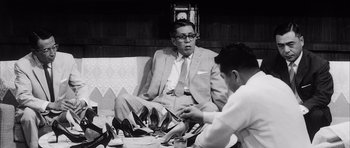 Movie still from “High and Low” (1963), directed by Akira Kurosawa – A man sitting on top of a couch next to another man; Medium shot, Low angle