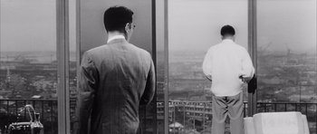 Movie still from “High and Low” (1963), directed by Akira Kurosawa – Two men are looking out a window at a city; Medium shot, Low angle