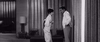 Movie still from “High and Low” (1963), directed by Akira Kurosawa – A man and a woman standing next to each other in front of a curtain; Wide shot, Low angle