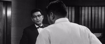Movie still from “High and Low” (1963), directed by Akira Kurosawa – A man in a suit and tie looking at another man in a dress shirt and bow tie; Medium shot, Over the shoulder angle