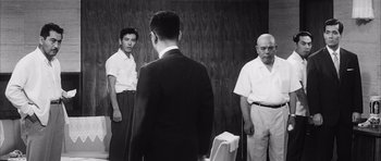 Movie still from “High and Low” (1963), directed by Akira Kurosawa – A group of men standing next to each other in front of a wooden wall; Medium shot, Over the shoulder angle