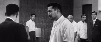 Movie still from “High and Low” (1963), directed by Akira Kurosawa – A man standing next to another man in front of a wall; Medium shot, Low angle