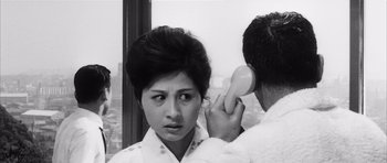 Movie still from “High and Low” (1963), directed by Akira Kurosawa – A woman looking in a mirror while a man is using a phone; Close Up shot, High angle