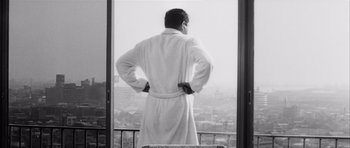 Movie still from “High and Low” (1963), directed by Akira Kurosawa – A man in a robe standing in front of a window looking out at a city; Medium shot, Low angle