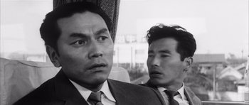 Movie still from “High and Low” (1963), directed by Akira Kurosawa – Two men in suits and ties are sitting next to each other; Close Up shot, Low angle