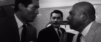Movie still from “High and Low” (1963), directed by Akira Kurosawa – A man in a suit and tie standing next to two other men; Medium shot, Low angle
