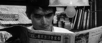 Movie still from “High and Low” (1963), directed by Akira Kurosawa – A young man reading a newspaper in a room; Close Up shot, Low angle