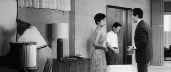 Movie still from “High and Low” (1963), directed by Akira Kurosawa – A woman standing next to a man in front of a wall; Wide shot, Low angle