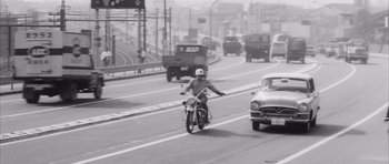 Movie still from “High and Low” (1963), directed by Akira Kurosawa – A man riding a motorcycle down the middle of a street; Wide shot, High angle