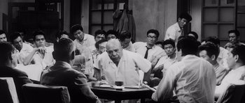 Movie still from “High and Low” (1963), directed by Akira Kurosawa – A group of people sitting around a table; Medium shot, Over the shoulder angle