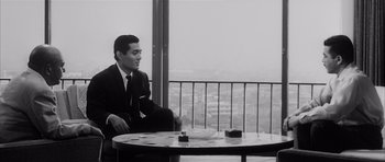 Movie still from “High and Low” (1963), directed by Akira Kurosawa – A black and white photo of a man sitting at a table; Medium shot, Over the shoulder angle