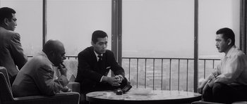 Movie still from “High and Low” (1963), directed by Akira Kurosawa – A black and white photo of a man sitting at a table; Medium shot, Low angle