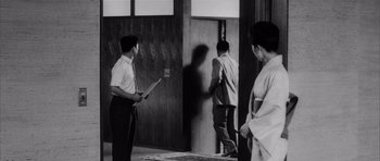 Movie still from “High and Low” (1963), directed by Akira Kurosawa – A group of people standing in front of a door; Wide shot, Over the shoulder angle