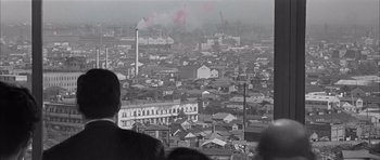Movie still from “High and Low” (1963), directed by Akira Kurosawa – A black - and - white photo of a city with smoke billowing from the chimney; Extreme Wide shot, High angle