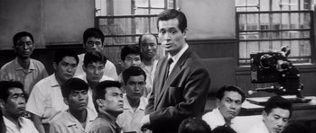 Movie still from “High and Low” (1963), directed by Akira Kurosawa – A man in a suit and tie standing in front of a group of people; Medium shot, High angle
