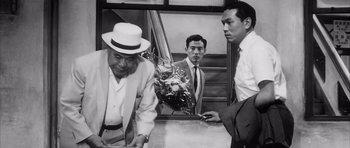 Movie still from “High and Low” (1963), directed by Akira Kurosawa – A man in a white suit and a man in a white suit and a man in a white suit and a man in a white suit; Medium shot, Low angle