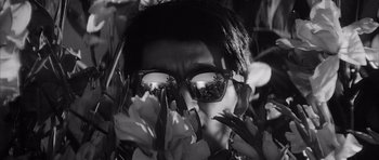 Movie still from “High and Low” (1963), directed by Akira Kurosawa – A man wearing sunglasses and hiding his face behind flowers; Extreme Close Up shot, Low angle