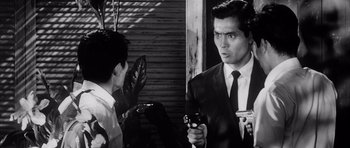 Movie still from “High and Low” (1963), directed by Akira Kurosawa – A man in a suit and tie holding a gun in his hand; Medium shot, Over the shoulder angle