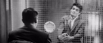 Movie still from “High and Low” (1963), directed by Akira Kurosawa – A man and a woman are in a jail cell; Medium shot, Over the shoulder angle