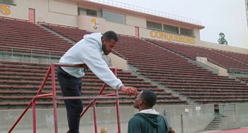 Movie still from “Higher Learning” (1995), directed by John Singleton – A man standing next to another man in a stadium; Medium shot, High angle