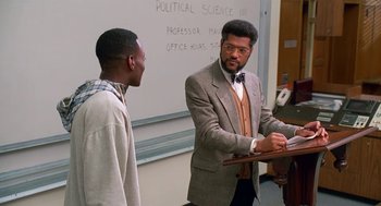 Movie still from “Higher Learning” (1995), directed by John Singleton – A man in a suit talking to a man in a tie in front of a desk; Medium shot, Over the shoulder angle
