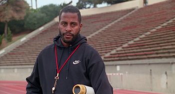 Movie still from “Higher Learning” (1995), directed by John Singleton – A man standing in front of an empty bleachers; Close Up shot, High angle