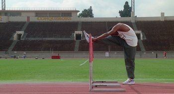 Movie still from “Higher Learning” (1995), directed by John Singleton – A man standing on one leg leaning over a hurdle; Wide shot, Low angle