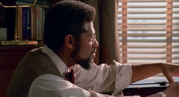 Movie still from “Higher Learning” (1995), directed by John Singleton – A man sitting at a table with his hand on his chin; Close Up shot, Over the shoulder angle