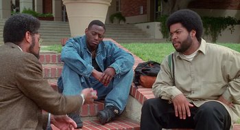 Movie still from “Higher Learning” (1995), directed by John Singleton – Two men sitting on a brick wall and one man is handing something to another man; Medium shot, High angle