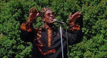 Movie still from “Higher Learning” (1995), directed by John Singleton – A man in a black and orange shirt is singing; Medium shot, Low angle