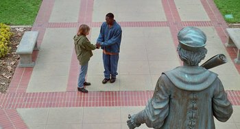Movie still from “Higher Learning” (1995), directed by John Singleton – Two people shaking hands in a courtyard with a statue in the background; Wide shot, High angle
