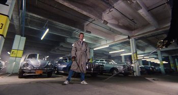 Movie still from “Highlander” (1986), directed by Russell Mulcahy – A man in a trench coat in a parking garage; Wide shot, Low angle