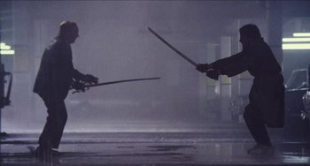 Movie still from “Highlander” (1986), directed by Russell Mulcahy – Two people are fighting with swords in the rain; Wide shot, Low angle