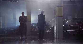 Movie still from “Highlander” (1986), directed by Russell Mulcahy – Two people in a parking garage with a car in the background; Wide shot, Low angle