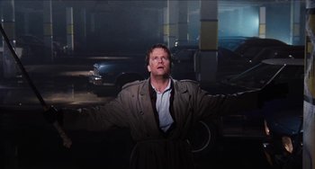 Movie still from “Highlander” (1986), directed by Russell Mulcahy – A man standing in a parking lot with his arms outstretched; Medium shot, Low angle
