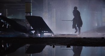 Movie still from “Highlander” (1986), directed by Russell Mulcahy – A person holding a sword while standing in the rain; Wide shot, Low angle