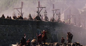 Movie still from “Highlander” (1986), directed by Russell Mulcahy – A group of people standing on top of a stone wall; Extreme Wide shot, Low angle
