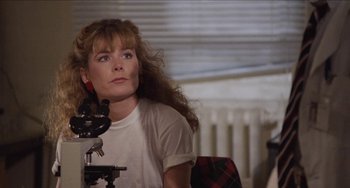 Movie still from “Highlander” (1986), directed by Russell Mulcahy – A woman sitting in front of a microscope looking up; Close Up shot, Over the shoulder angle