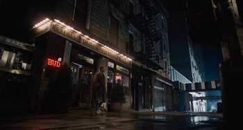 Movie still from “Highlander” (1986), directed by Russell Mulcahy – A man walking down the street in front of a building at night; Wide shot, Low angle