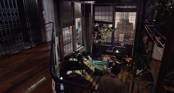Movie still from “Highlander” (1986), directed by Russell Mulcahy – A man sitting in a living room next to a window; Wide shot, High angle