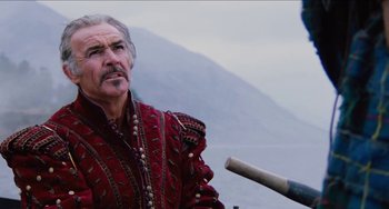 Movie still from “Highlander” (1986), directed by Russell Mulcahy – An older man in a red and black outfit holding a sword; Close Up shot, Low angle